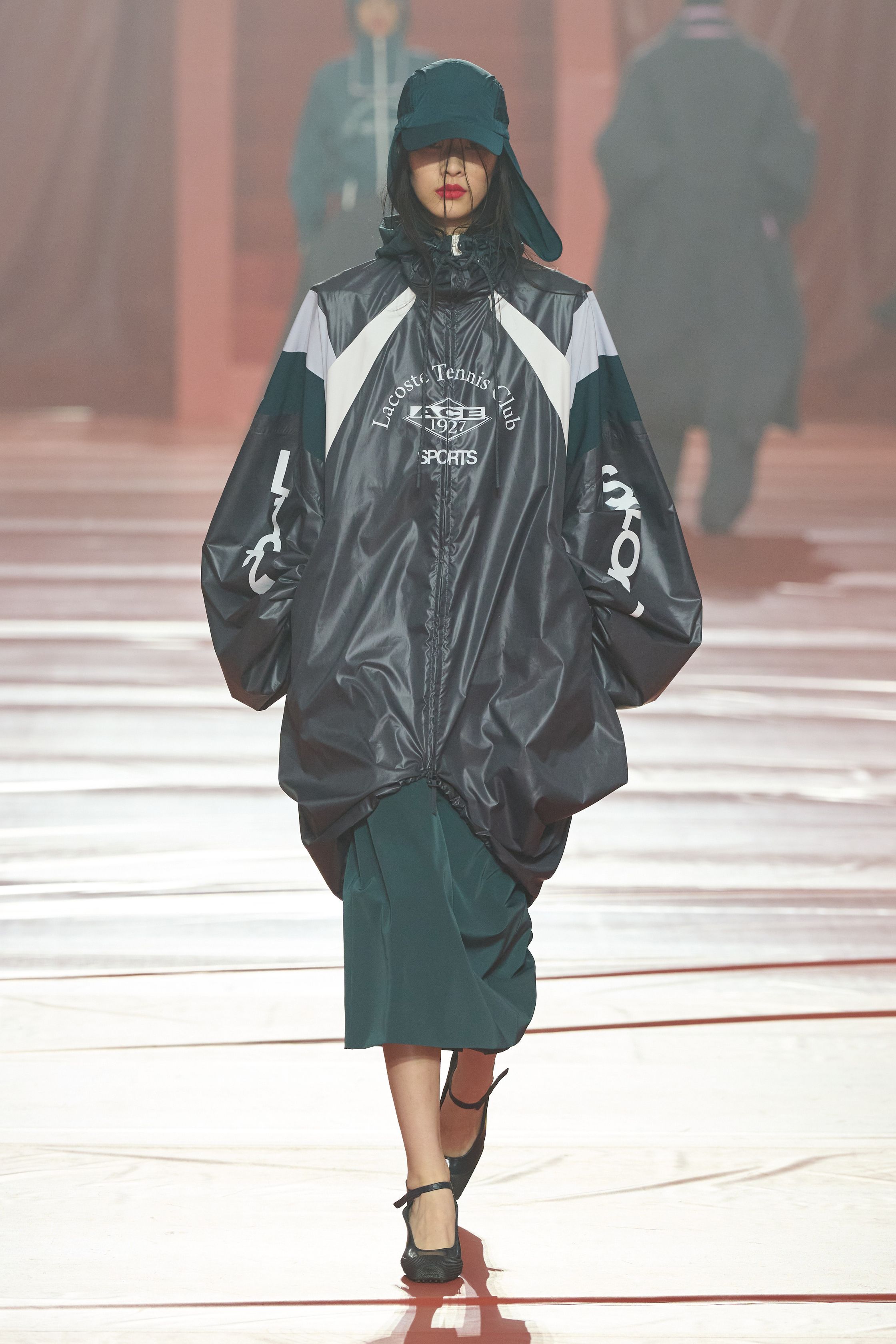 这一季 Lacoste 将品牌最核心的运动基因彻底升级为都市机能时装：酒红色尼龙运动外套、宽体运动裙、拉链高领和oversize运动风衣贯穿整场，经典网球白与深绿被重新调和成更成熟的学院运动色谱。轮廓保持宽松与机能感，但通过女性化中长裙、修身针织和高跟鞋完成优雅转换，使运动不再只是休闲，而是城市女性的日常盔甲-顽石频道趋势研究